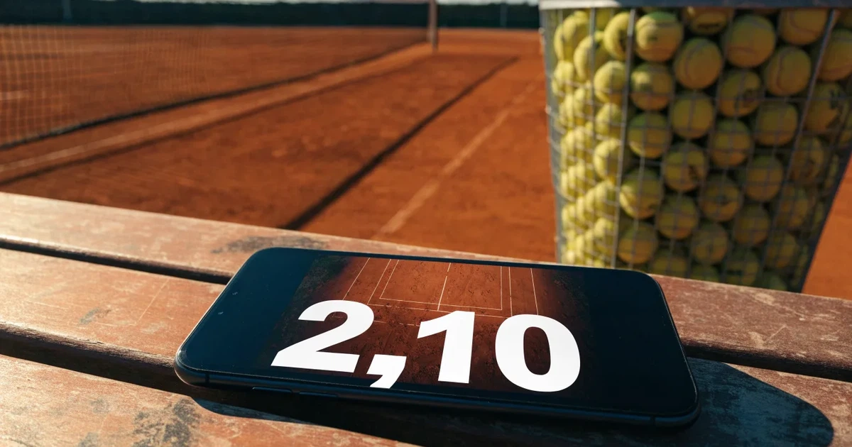Ein Sandplatz mit frisch gezogenen Linien in der Nachmittagssonne, Netz und Ballkorb am Rand, keine Menschen.