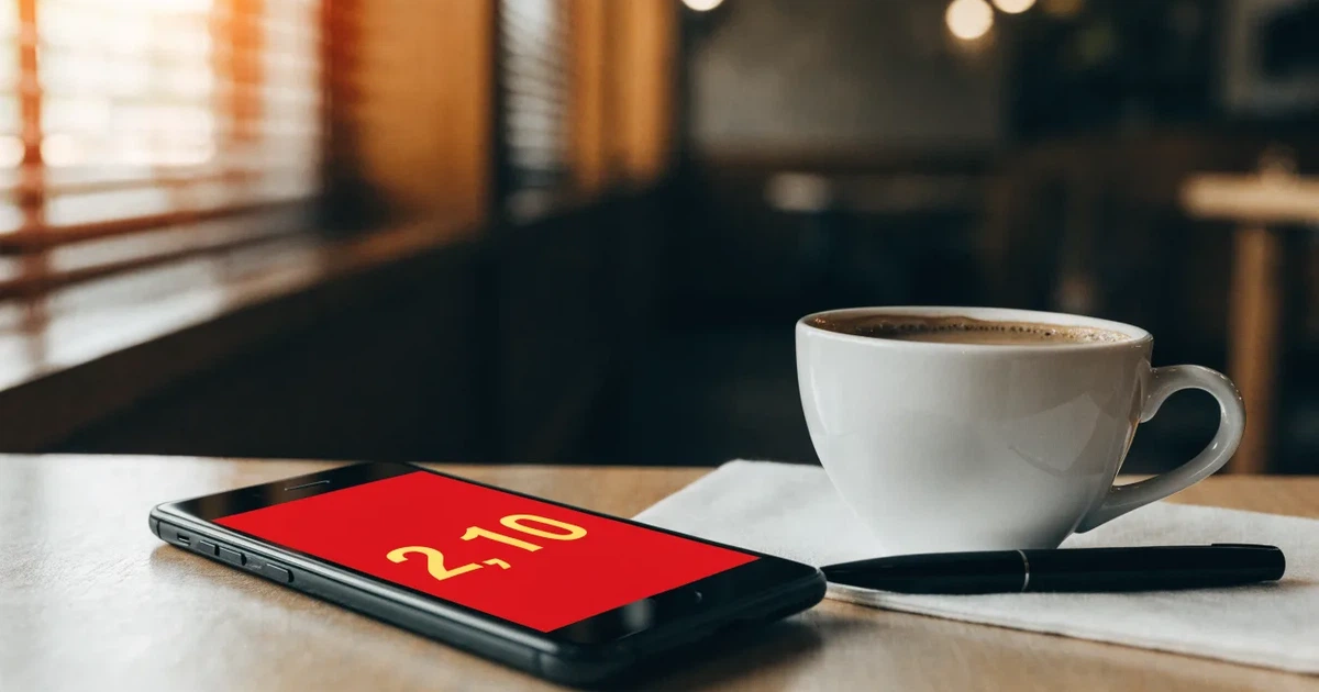Ein Smartphone liegt mit dunklem Display auf einem Café-Tisch neben einer Tasse Kaffee und einem Kugelschreiber.