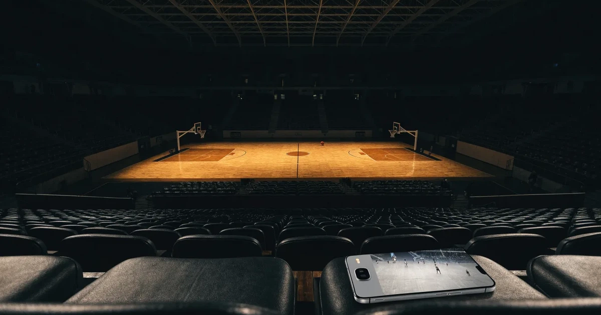 Eine leere Basketballhalle von einer oberen Tribünenreihe aus gesehen, Parkett und Körbe im Licht der Hallenstrahler.