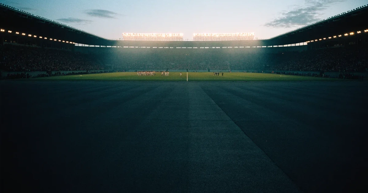 Ein Fußballstadion unter Flutlicht aus großer Entfernung, davor ein dunkler Parkplatz und ein heller Abendhimmel.