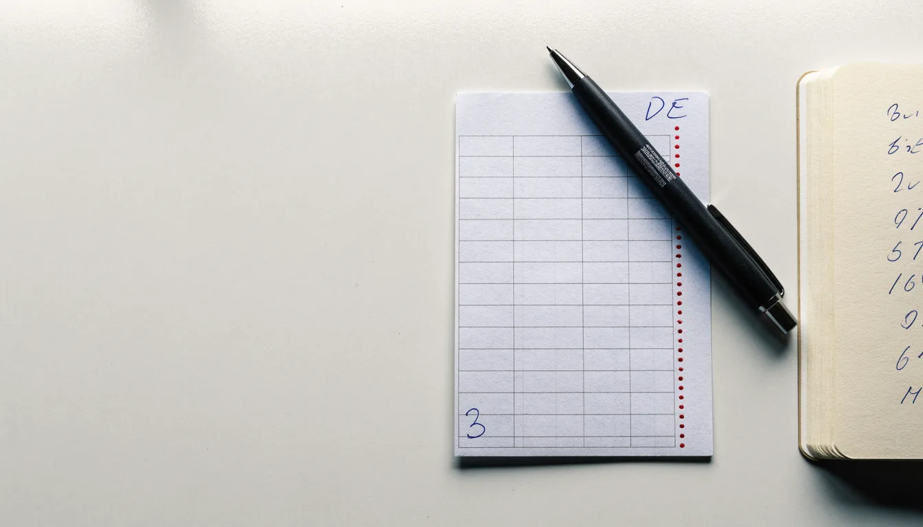 Ein leerer Papierwettschein und ein Kugelschreiber auf einer glatten Schreibtischplatte, daneben ein aufgeschlagenes Notizbuch mit handschriftlichen Notizen.