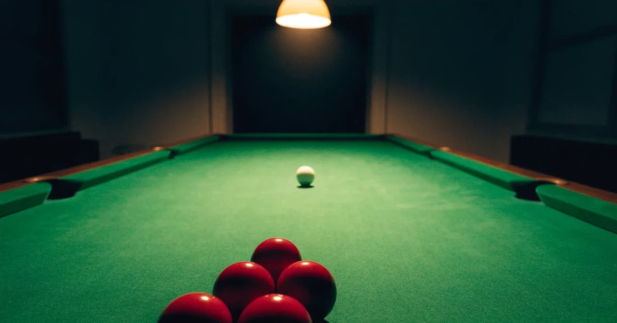 Ein Snookertisch mit grünem Tuch und aufgebauten roten Kugeln in einem abgedunkelten Raum unter einer hängenden Lampe.